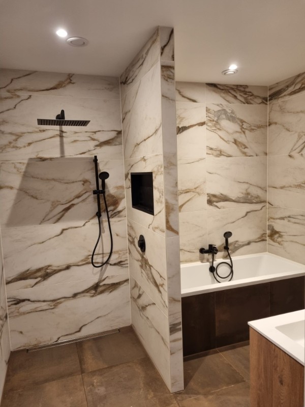 Marmerlook badkamer met zwarte regendouche en ligbad, uitgevoerd door Vrolijk Klusbedrijf
